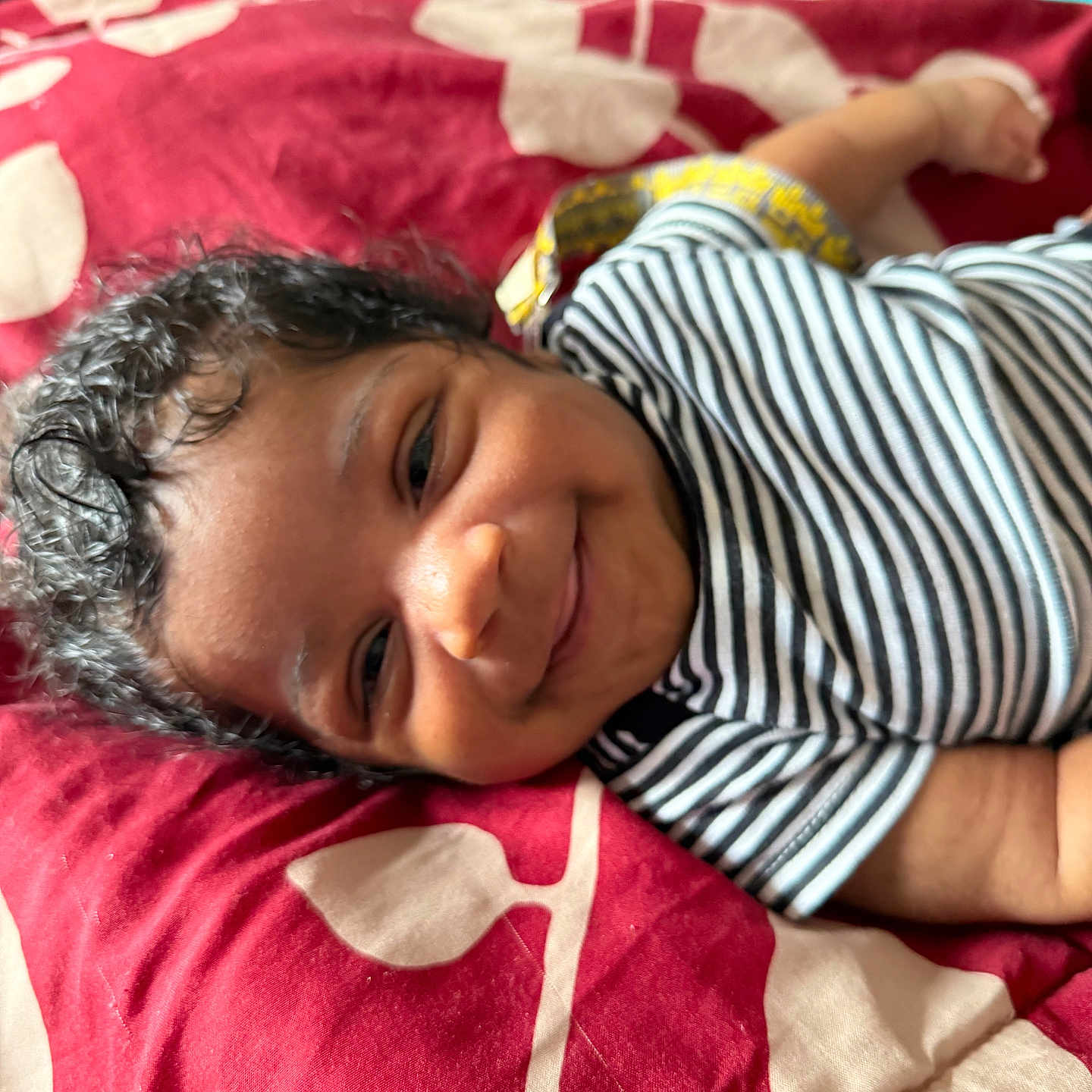 Sincere joined the competition — help win amazing prizes! baby, beige_pattern, blanket, child, close_up, cozy, curly_hair, cute, face, happy, indoors, infant, lying_down, person, portrait, red_blanket, smiling, soft_lighting, striped_shirt, young_child