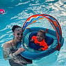 baby, child, adult, woman, smiling, swimming_pool, water, floating_raft, pool_float, life_ring, orange_shirt, swimwear, outdoor, family, portrait, summer, recreation, water_safety, poolside, happy