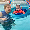 adult, baby, child, swimming_pool, pool_float, inflatable_float, water, outdoor, summer, family, father, parent, smiling, portrait, wet_hair, orange_shirt, blue_water, backyard, poolside, recreation