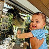 Zakiah is registered to the contest to win money with this photo: baby, child, monkey, zoo, animal, wildlife, glass, enclosure, outdoor, portrait, smiling, happy, blue_clothing, infant, adult, holding, reaching, face, primate, family