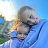 child, children, sibling_love, hug, embrace, curly_hair, outdoor, sky, blue_sky, sweatshirt, purple_clothing, portrait, happy, smile, cute, affection, family, young_child, close_up, daylight