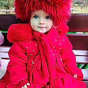 Lily is registered to the contest to win money with this photo: child, toddler, red_coat, red_hat, scarf, outdoor, bench, winter_clothing, blue_eyes, portrait, cute, warm_clothing, nature_background, seasonal, fashion, person, face, sitting, cold_weather, fur_trim