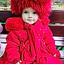 child, toddler, red_coat, red_hat, scarf, outdoor, bench, winter_clothing, blue_eyes, portrait, cute, warm_clothing, nature_background, seasonal, fashion, person, face, sitting, cold_weather, fur_trim