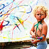 Adam is registered to the contest to win money with this photo: art, background, barefoot, body_paint, canvas, child, colorful, creative, curly_hair, expression, fun, messy, outdoor, paint, paintbrush, playtime, portrait, shorts, summer, toddler