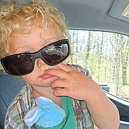 Adam is registered to the contest to win money with this photo: blue_plush, car_interior, casual, child, curly_hair, expression, face, forest, green_shirt, hand, indoors, nose, plaid_shirt, seat, stuffed_animal, sunglasses, sunlight, toddler, trees, window