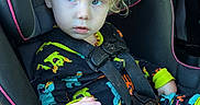 Adam joined the competition — help win amazing prizes! child, toddler, car_seat, curly_hair, blue_eyes, pajamas, dinosaur_pattern, seat_belt, car_interior, sitting, clothing, young_child, cute, indoors, safety, portrait, expression, daylight, seat, baby