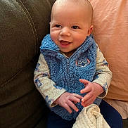 Cooper is registered to the contest to win money with this photo: baby, blanket, blue_vest, child, clothing, couch, cozy, cute, fabric, hands, happy, indoor, infant, person, pillow, portrait, seated, smiling, soft_lighting, young_child