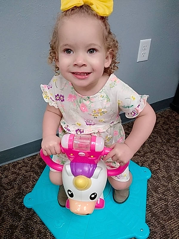Desleigh is registered to the contest to win money with this photo: arm, baby, baby_toddler_clothing, cheek, chin, dress, face, facial_expression, hairstyle, head, joy, organ, person, pink, product, purple, skin, sleeve, smile, toy