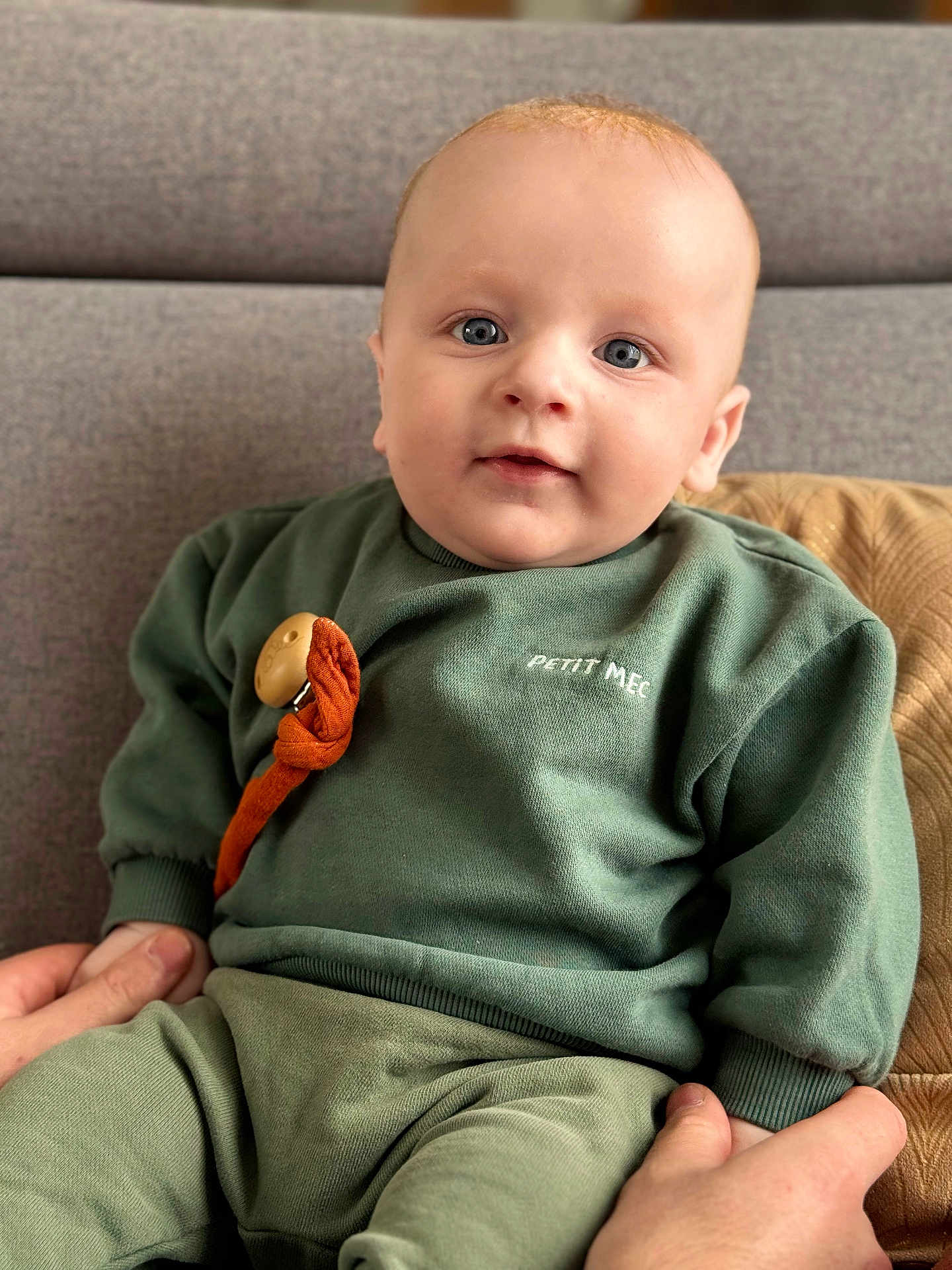 Loann a rejoint le concours — aidez-le/la à gagner de superbes lots ! baby, child, face, person, couch, clothing, green_sweater, pants, hand, indoor, portrait, cute, seated, soft_furniture, home, expression, skin, eyes, sitting, comfort