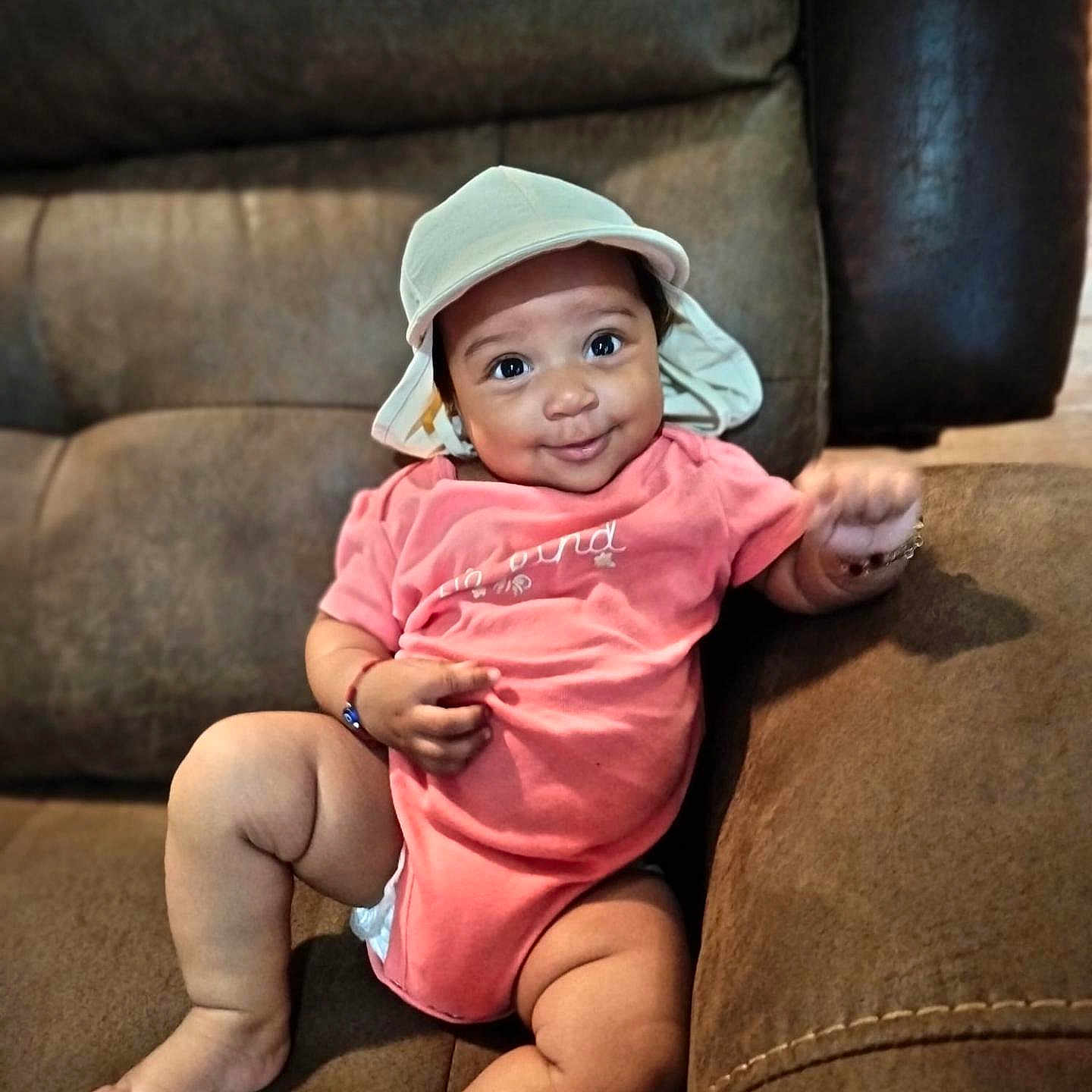 Sade Zanarielle joined the competition — help win amazing prizes! arm, baby, bracelet, child, chubby, couch, cute, face, furniture, happy, hat, indoors, infant, legs, pink_onesie, portrait, relaxed, seated, skin, smile