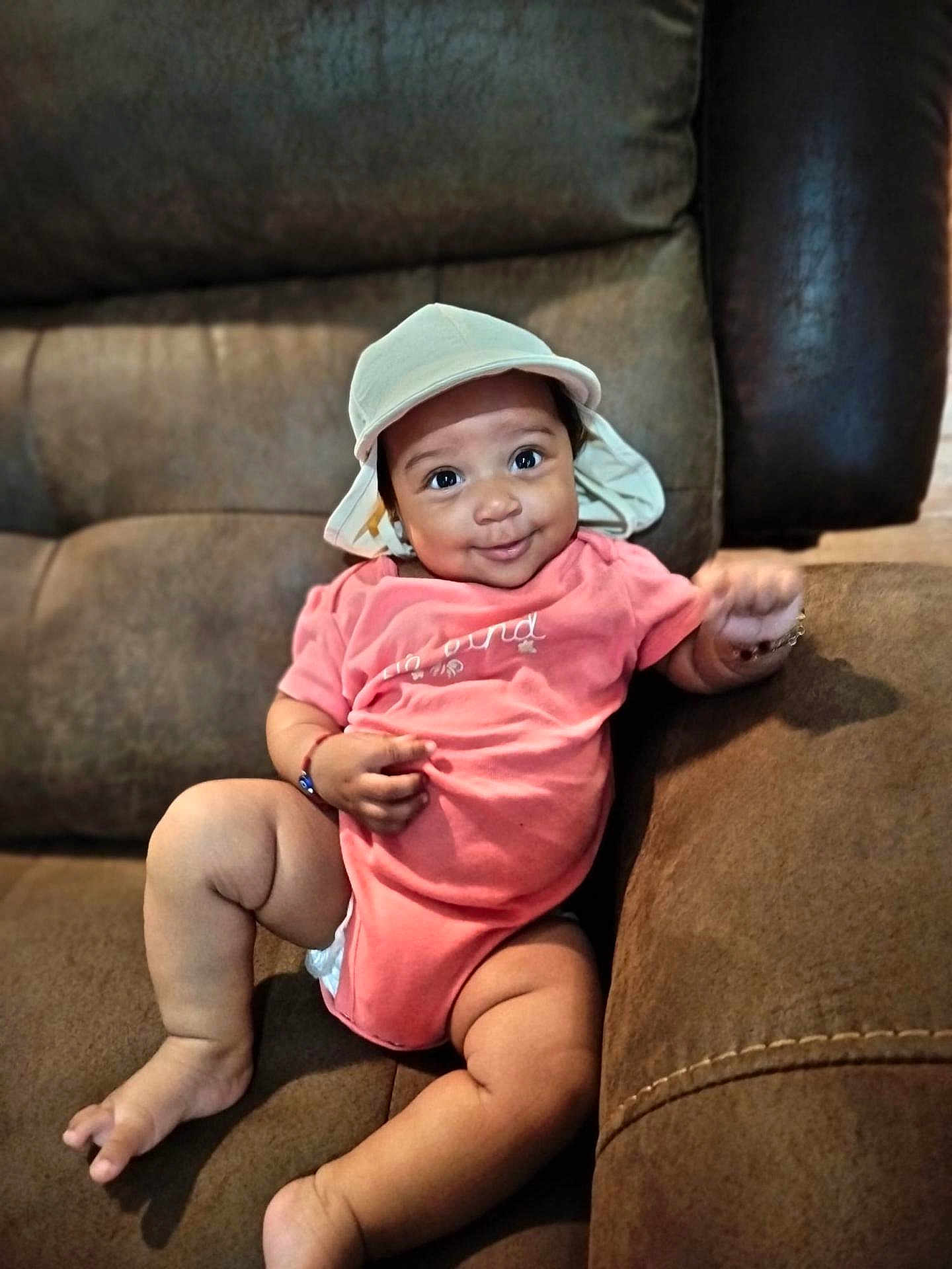 Sade Zanarielle joined the competition — help win amazing prizes! baby, infant, child, hat, pink_onesie, couch, furniture, smile, cute, chubby, indoors, skin, face, legs, arm, bracelet, relaxed, seated, happy, portrait