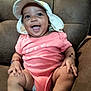 baby, child, smiling, hat, pink_onesie, sitting, brown_chair, happy, cute, infant, indoors, furniture, portrait, skin, legs, feet, hands, bracelet, person, expression