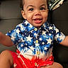 toddler, child, smiling, happy, sitting, blue_shirt, red_shorts, stars_pattern, indoor, couch, blanket, curly_hair, cute, baby, person, portrait, clothing, skin, foot, buttoned_shirt