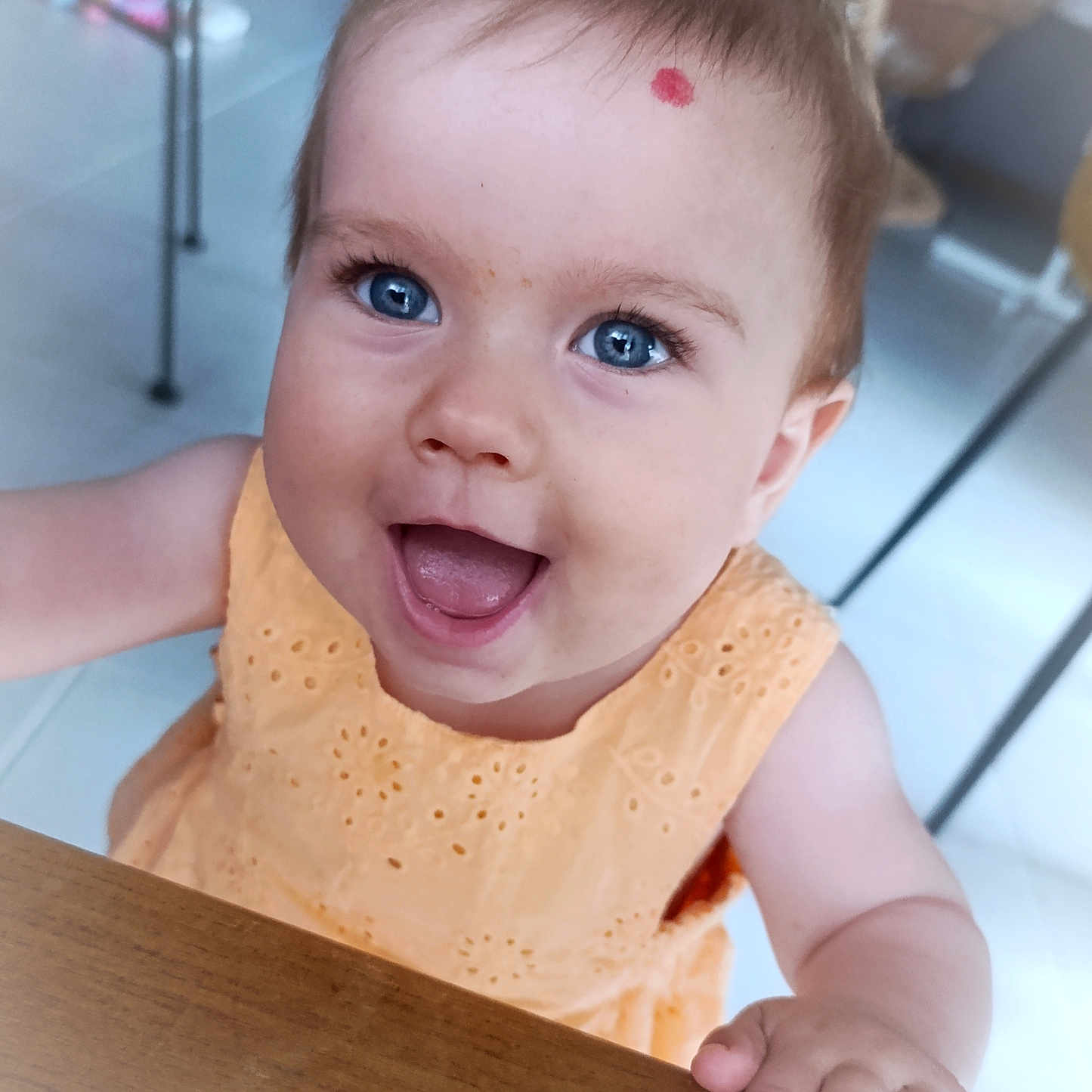 Athénays participe au concours pour gagner de l'argent avec cette photo : baby, blue_eyes, bright, child, curly_hair, cute, expression, face, hand, happy, indoor, infant, looking_up, orange_dress, person, portrait, skin, smiling, table, young