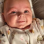 baby, cat_prints, child, chubby_cheeks, close_up, cozy, cute, cute_expression, face, happy, indoors, infant, lying_down, newborn, onesie, person, portrait, sleepwear, smiling, soft_lighting