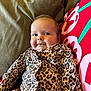 apparel, baby, child, clothing, comfortable, cozy, cushion, cute, face, green, indoor, infant, leopard_print, person, pillow, portrait, red, resting, smile, young