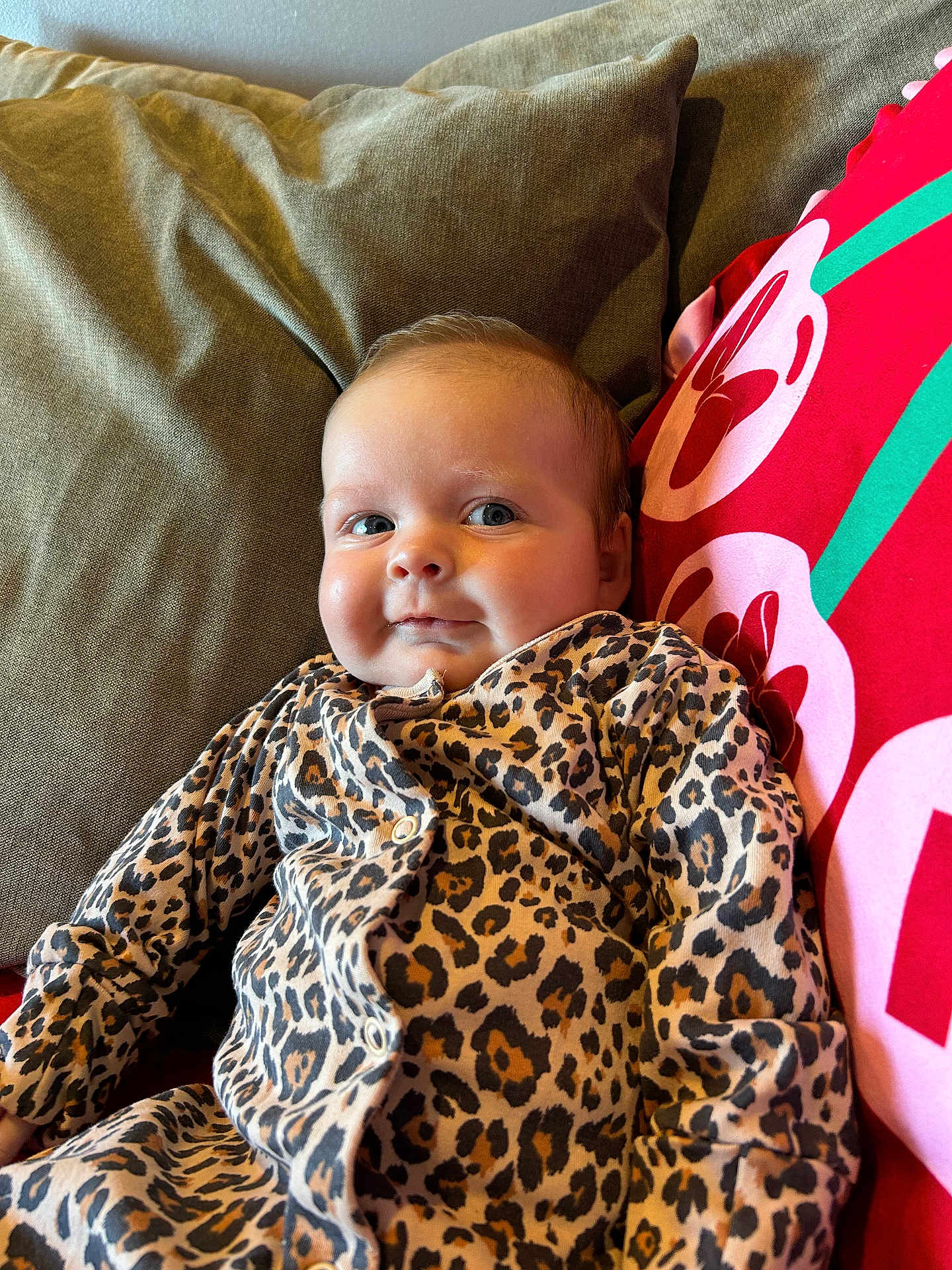 Naveah joined the competition — help win amazing prizes! apparel, baby, child, clothing, comfortable, cozy, cushion, cute, face, green, indoor, infant, leopard_print, person, pillow, portrait, red, resting, smile, young