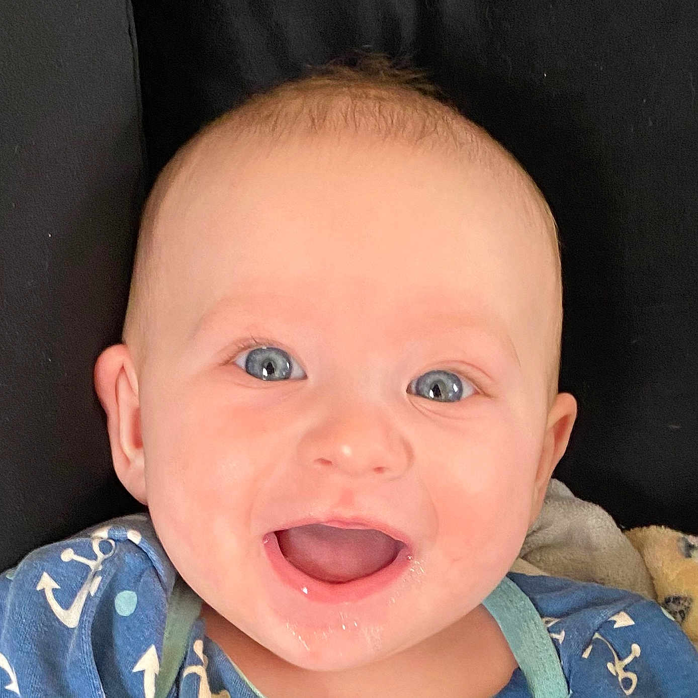 Noah is registered to the contest to win money with this photo: anchor_pattern, baby, baby_boy, background, blue_eyes, blue_outfit, child, closeup, clothing, cute, expression, face, happy, head, indoors, infant, mouth_open, person, skin, smiling