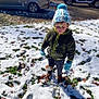 child, snow, winter_clothing, hat, gloves, jacket, pants, boots, outdoor, daylight, car, grass, leaf, footprint, cold_weather, parked_vehicle, street, person, young_child, winter