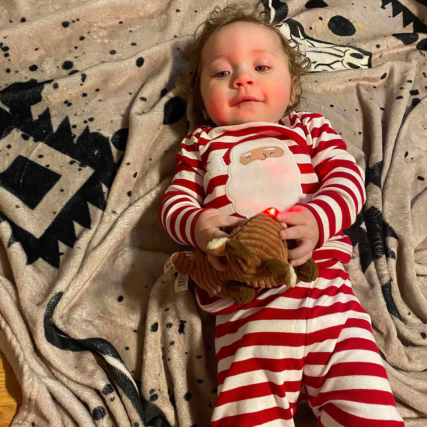 Liliana Rose Kinder is registered to the contest to win money with this photo: baby, blanket, child, curly_hair, cute, face, floor, holding, holiday_theme, indoor, infant, lying_down, pajamas, patterned_blanket, person, plush_toy, red, striped_clothing, toy, white