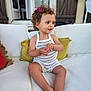child, toddler, curly_hair, hair_clip, white_couch, cushion, knitted_romper, striped_clothing, barefoot, indoors, window, door, wooden_shutters, smiling, portrait, sitting, cute, expression, skin, furniture