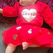 Amanda joined the competition — help win amazing prizes! baby, infant, newborn, red_dress, heart_graphic, loved_text, tulle_skirt, bare_foot, face, cheek, pillow, velvet_background, bed, blanket, indoor, portrait, cute, sleepy_expression, arm, leg