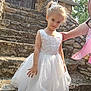 Wendy participe au concours pour gagner de l'argent avec cette photo : child, cute, daylight, fashion, girl, hair_accessory, hand, happy, nature, outdoor, person, portrait, smiling, standing, stone_steps, stone_wall, sunlight, white_dress, wooden_door, young