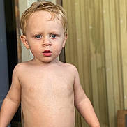 Trevor is registered to the contest to win money with this photo: toddler, child, shirtless, blonde_hair, blue_eyes, curious, standing, indoors, door, wooden_wall, skin, young_child, portrait, expression, casual, natural_light, human, person, face, bare_chest