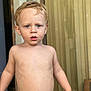 toddler, child, shirtless, blonde_hair, blue_eyes, curious, standing, indoors, door, wooden_wall, skin, young_child, portrait, expression, casual, natural_light, human, person, face, bare_chest