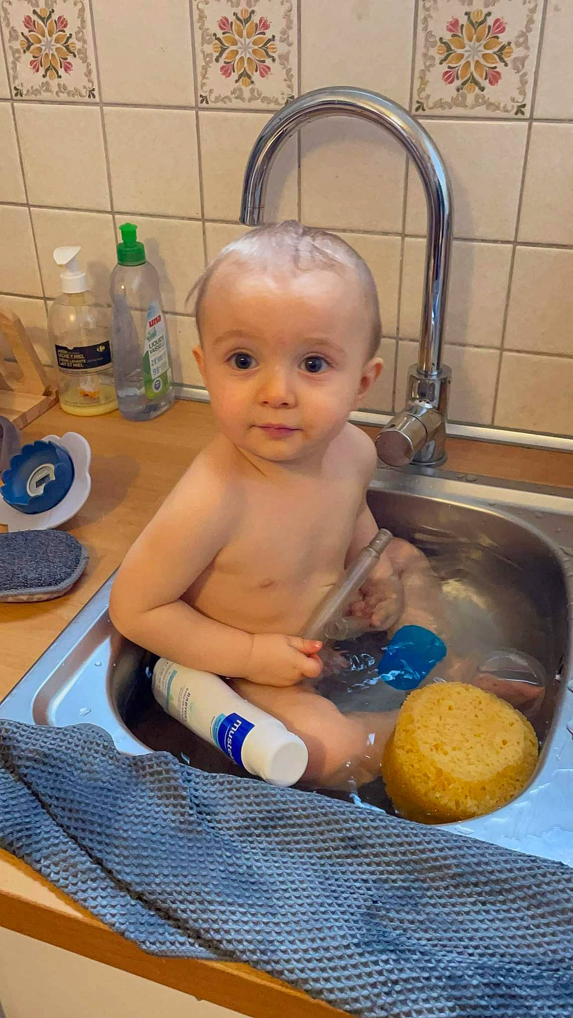 Maé a rejoint le concours — aidez-le/la à gagner de superbes lots ! arm, baby, baby_products, bathing, bathroom, bottle, cheek, chest, child, eye, human_body, mouth, person, personal_care, plumbing, plumbing_fixture, sink, tap, toddler, toy