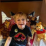 child, boy, smiling, indoor, stuffed_animals, winnie_the_pooh, monkey_toy, blanket, fort, casual_clothing, jeans, black_tshirt, toys, playtime, happy, cute, seated, teddy_bear, plush_toys, childhood
