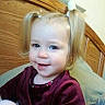 toddler, child, smile, pigtails, blonde_hair, maroon_clothing, wooden_headboard, pillow, indoor, face, portrait, person, baby, cute, young_child, sitting, happy, home, casual, closeup