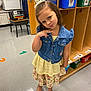 box, child, clothing, desk, face, female, footwear, furniture, girl, hair, head, jeans, pants, person, sandal, shoe, shorts, sleeve, standing, student