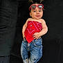 baby, child, sunglasses, red_bandana, jeans, socks, pigtails, black_couch, cute, smiling, fashion, casual_wear, indoor, portrait, person, happy, young_child, accessories, footwear, relaxed