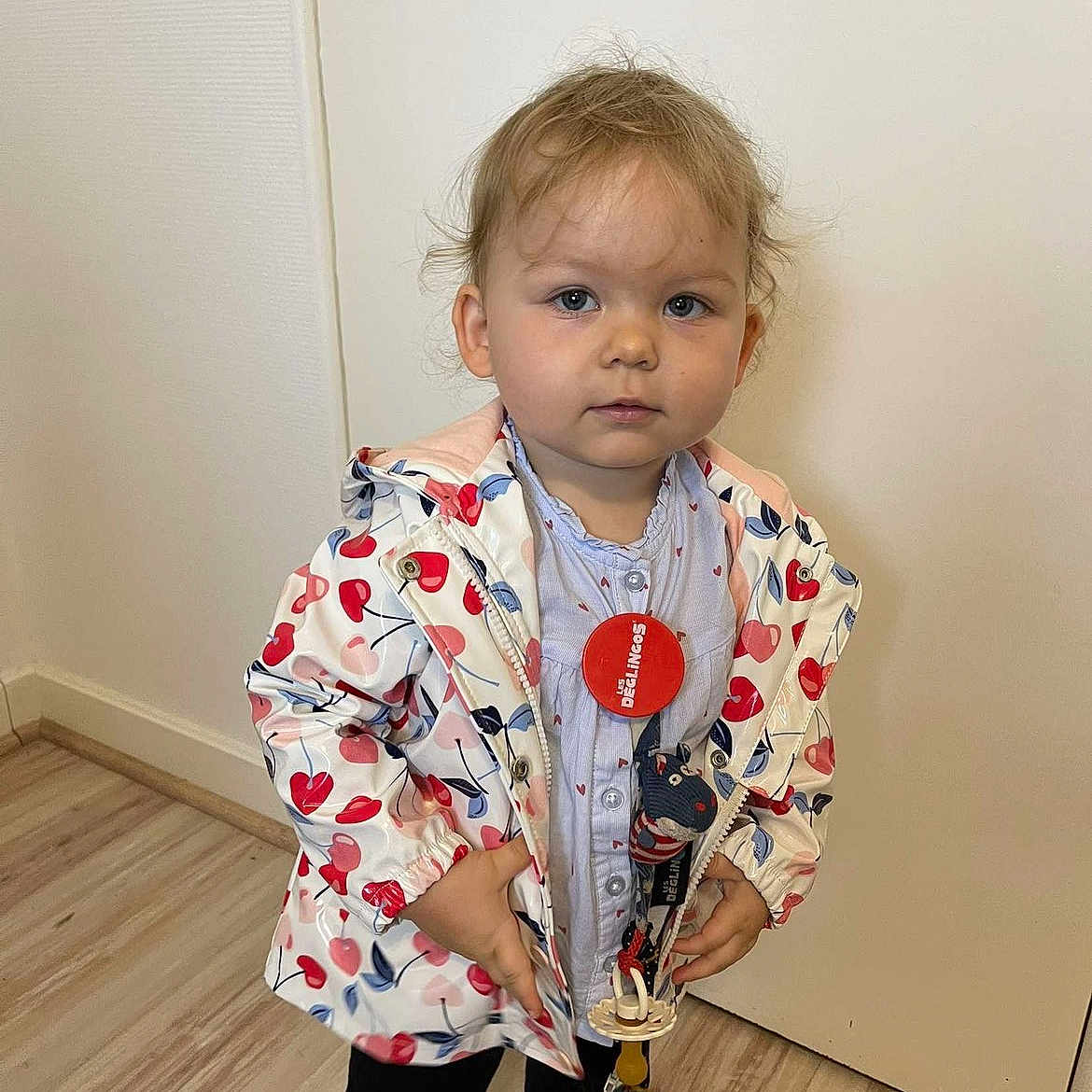 Livya participe au concours pour gagner de l'argent avec cette photo : accessory, casual, child, clothing, expression, face, floor, footwear, hair, heart_pattern, indoor, jacket, looking_at_camera, pacifier, person, standing, toddler, toy, wall, young_child