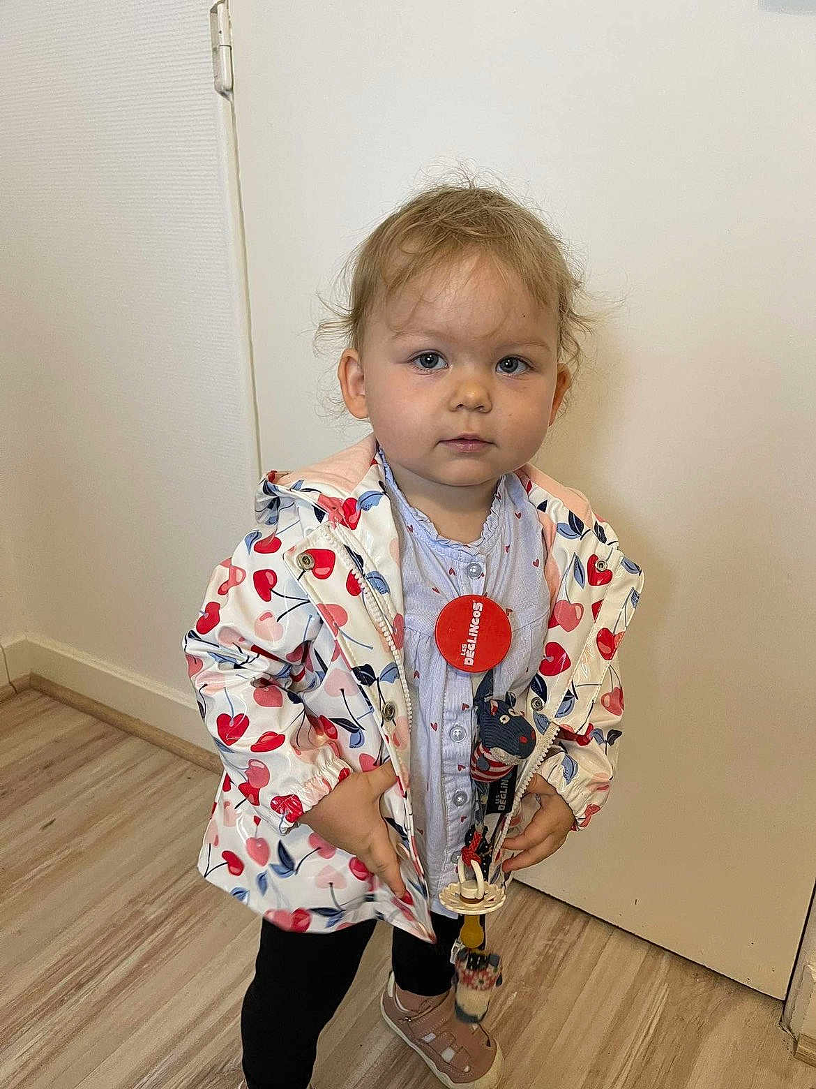 Livya participe au concours pour gagner de l'argent avec cette photo : accessory, casual, child, clothing, expression, face, floor, footwear, hair, heart_pattern, indoor, jacket, looking_at_camera, pacifier, person, standing, toddler, toy, wall, young_child