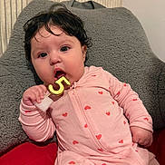 Abigail Latorre is registered to the contest to win money with this photo: baby, infant, child, portrait, face, wide_eyed, curly_hair, sitting, lying_down, pink_outfit, heart_pattern, onesie, teething_toy, gold_number, cushion, blanket, indoor, cozy, close_up, happy