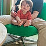 Romy a rejoint le concours — aidez-le/la à gagner de superbes lots ! adult, baby, black_shirt, carpet, casual_clothing, child, cute, furniture, green_chair, happy, holding, indoor, legs, natural_light, pants, person, seated, smiling, table, toddler
