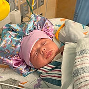 Aleiah is registered to the contest to win money with this photo: newborn, baby, sleeping, hospital, blanket, bonnet, unicorn, rainbow, medical_equipment, wires, dinosaur_print, bed, face, clothing, infant, cute, resting, child, wrapped, indoors