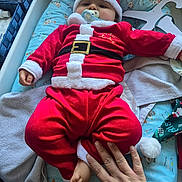 Myllan participe au concours pour gagner de l'argent avec cette photo : baby, santa_outfit, pacifier, hand, foot, changing_pad, blanket, clothing, bed, infant, holiday, red, white, fur_trim, cute, indoors, person, child, festive, smile