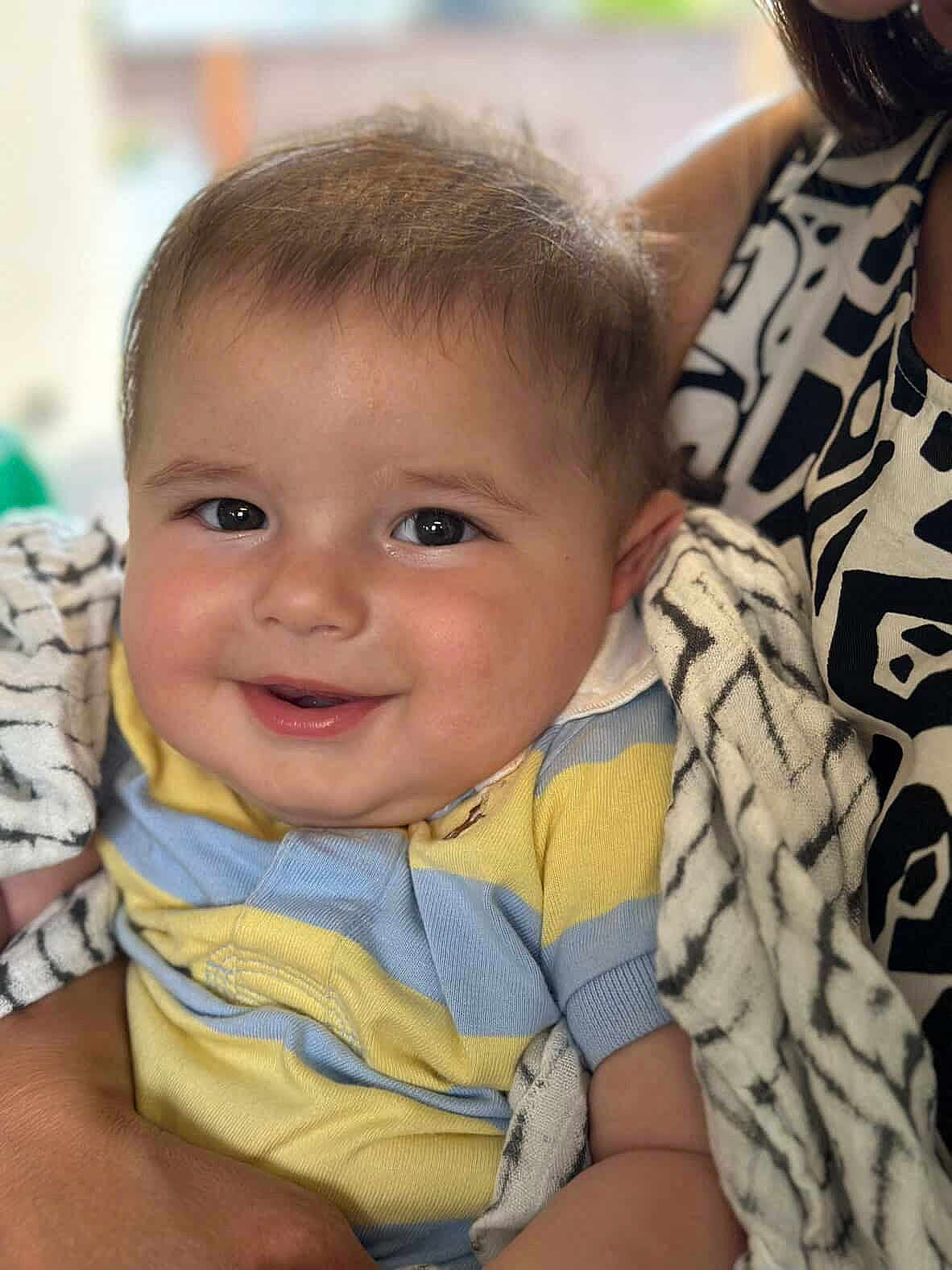 Alex is registered to the contest to win money with this photo: baby, smiling, child, blanket, striped_shirt, person, face, cheeks, arm, holding, patterned_clothing, adult, close_up, indoor, soft_light, happy, cute, portrait, infant, comfort