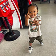 Keyontae is registered to the contest to win money with this photo: child, smiling, braids, indoor, nike, sneakers, tiled_floor, candy_dispenser, stroller, clothing, person, happy, young_child, standing, playful, casual_wear, footwear, retail, floor, portrait