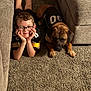 boy, child, glasses, dog, pet, carpet, couch, indoor, smiling, lying_down, black_jersey, matching_outfits, home, cozy, furniture, relaxed, cute, portrait, young, friendship