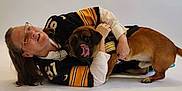 Bear is registered to the contest to win money with this photo: woman, dog, glasses, hugging, sports_jersey, playful, lying_down, tongue_out, pet, casual, indoor, brown_dog, happy, smiling, matching_clothes, white_background, portrait, friendship, affection, candid