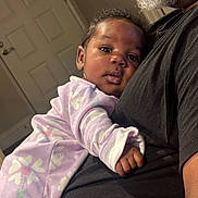 Leilani is registered to the contest to win money with this photo: adult, arm, baby, beard, black_shirt, close_up, cozy, curious_eyes, door, family, heart_pattern, holding, human, indoor, infant, onesie, portrait, purple_clothing, resting, skin