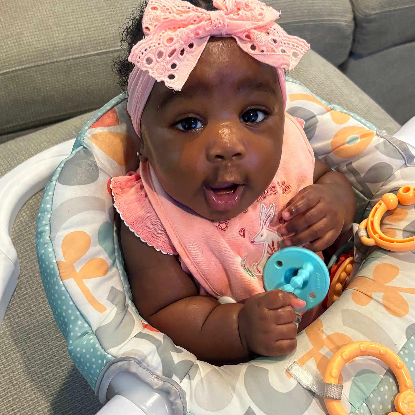 Leilani is registered to the contest to win money with this photo: activity_seat, adorable, baby, baby_toys, child, close_up, colorful, couch, curly_hair, happy, headband, home, indoor, infant, pink_bow, playtime, portrait, sitting, smiling, teether