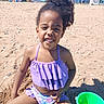 child, beach, sand, smiling, portrait, outdoor, sunny, purple_clothing, swimsuit, curly_hair, bucket, sandcastle, seaside, summer, playground, vacation, beachgoers, umbrella, house, happy