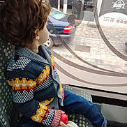 O H a rejoint le concours — aidez-le/la à gagner de superbes lots ! child, toddler, curly_hair, knitted_sweater, colorful_clothing, blue_jeans, white_shoes, red_ball, window, bus_seat, public_transport, side_view, urban_scene, car_outside, patterned_seat, indoor, daylight, casual, sitting, looking_out