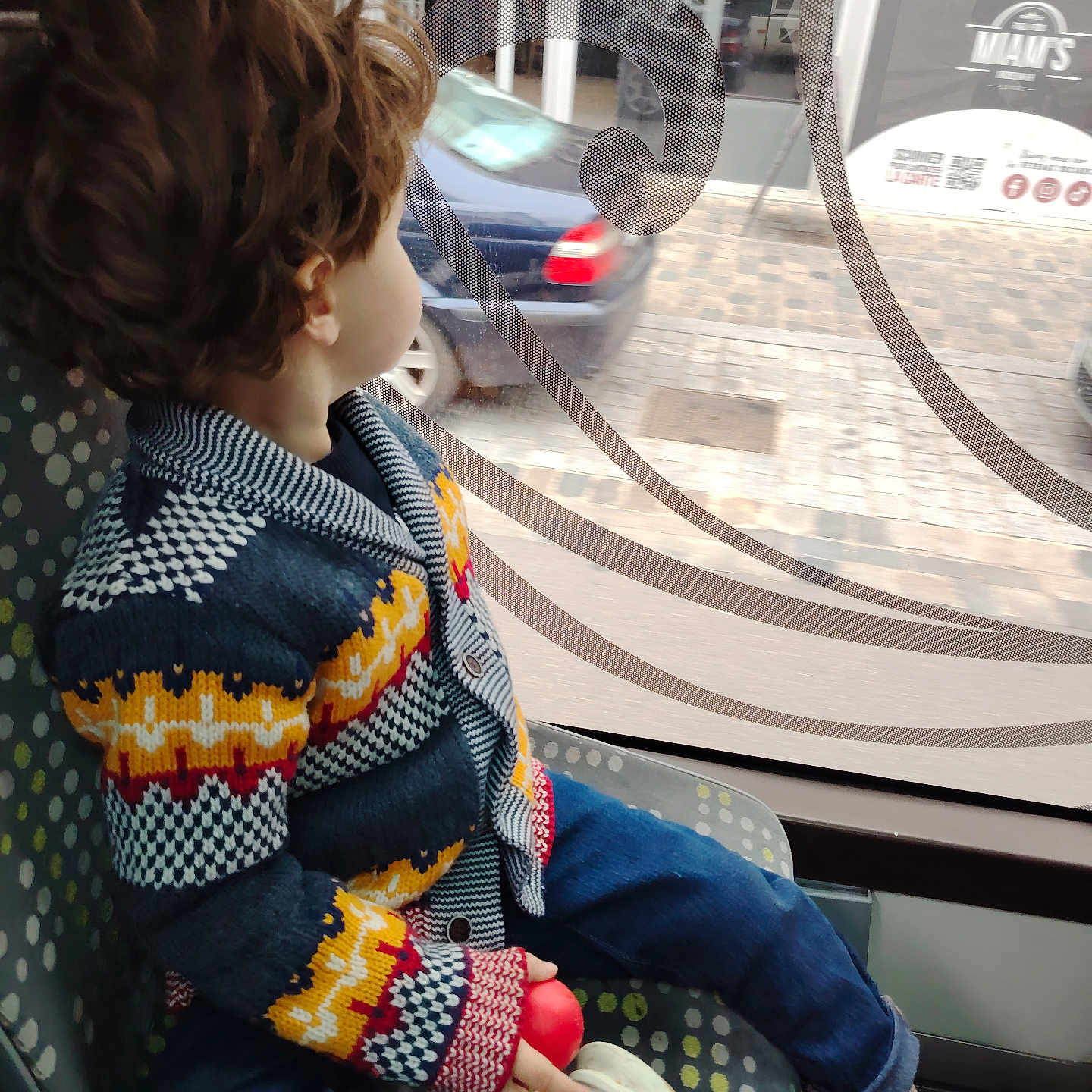 O H a rejoint le concours — aidez-le/la à gagner de superbes lots ! blue_jeans, bus_seat, car_outside, casual, child, colorful_clothing, curly_hair, daylight, indoor, knitted_sweater, looking_out, patterned_seat, public_transport, red_ball, side_view, sitting, toddler, urban_scene, white_shoes, window