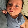 baby, infant, child, onesie, blue_clothing, person, face, skin, hand, arm, floor, tile, holding, caring, indoor, closeup, portrait, newborn, curious, soft_lighting